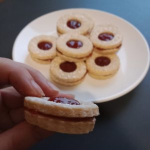 Des petits biscuits sablés rond à la confiture de fraise dans une assiette, et un biscuit sablé fourré en gros plan