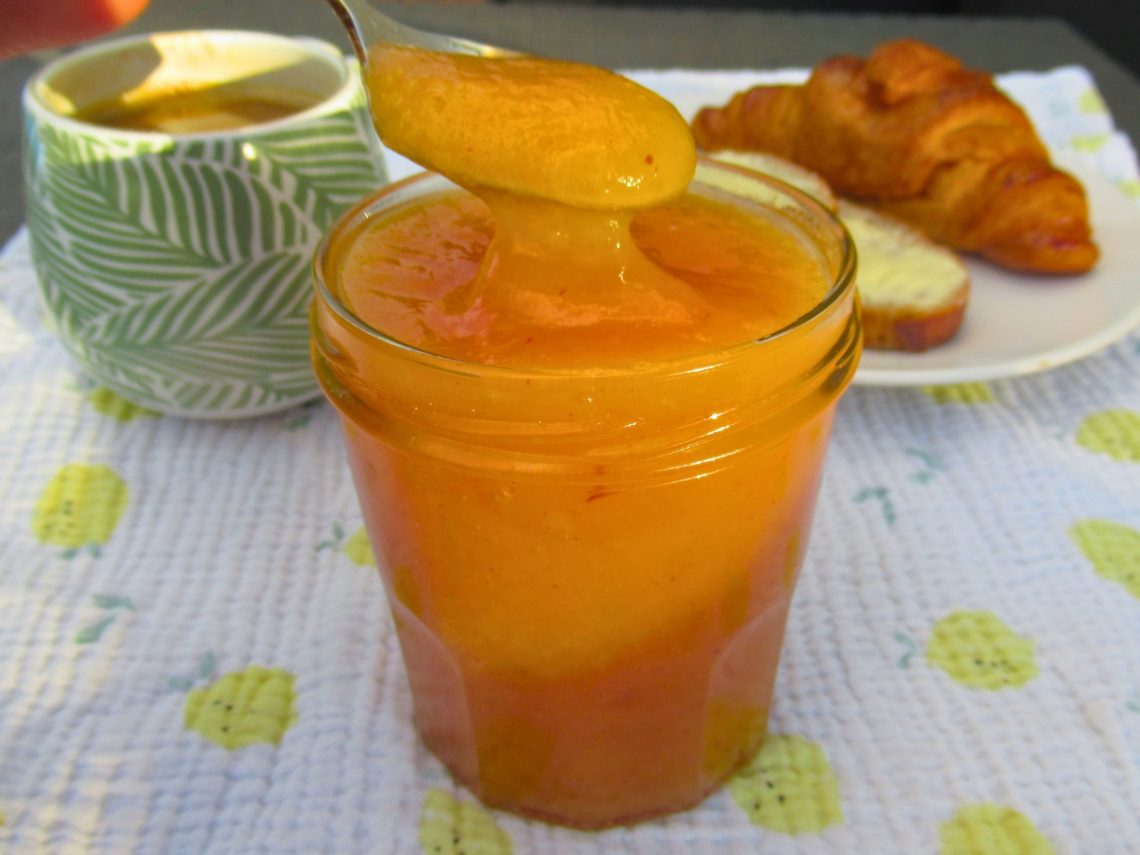 Pot de confiture de pêche de vigne maison avec une cuillère, servi avec un croissant et un café